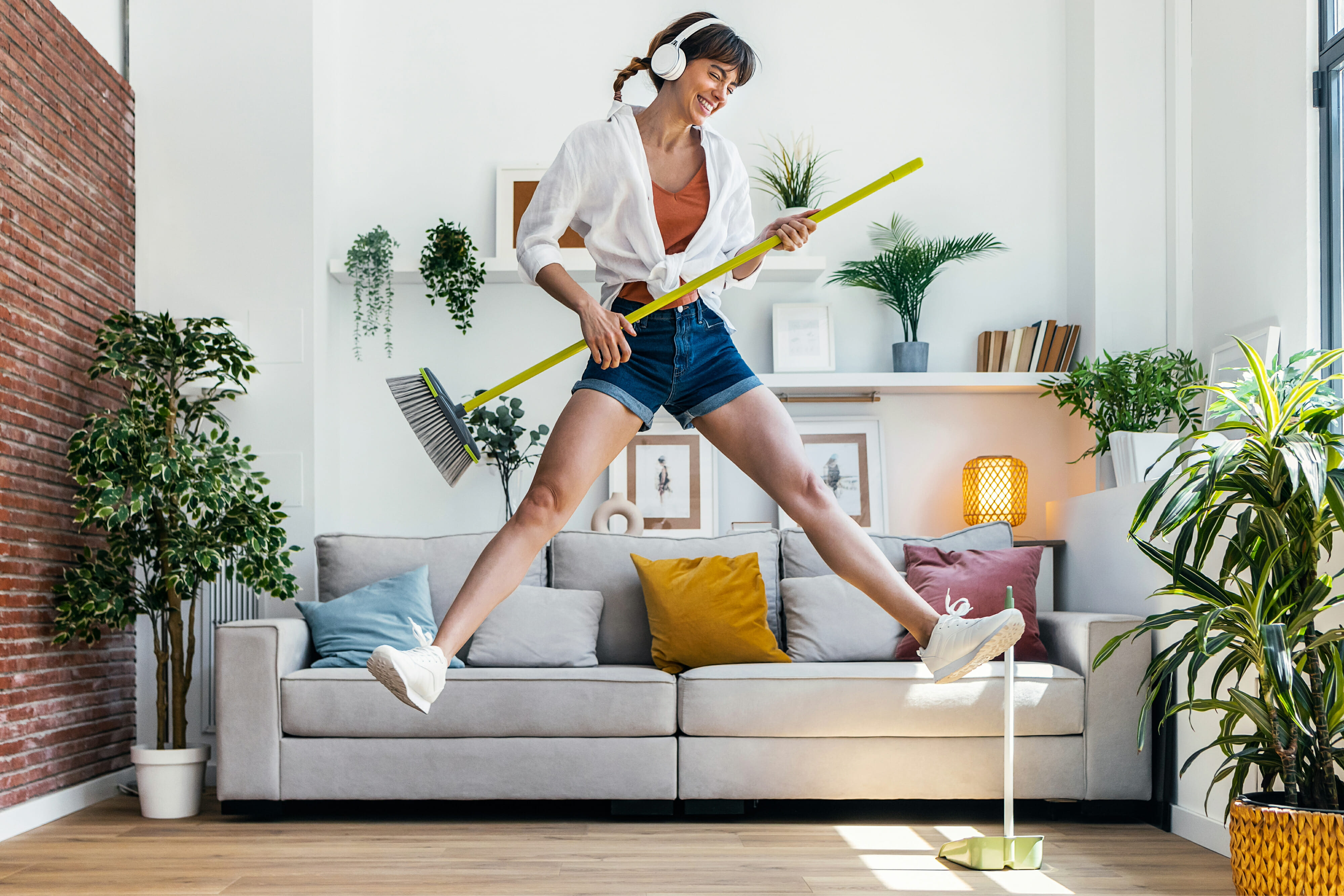 Funny motivated woman dancing and listening to music with headphones while sweeping the house