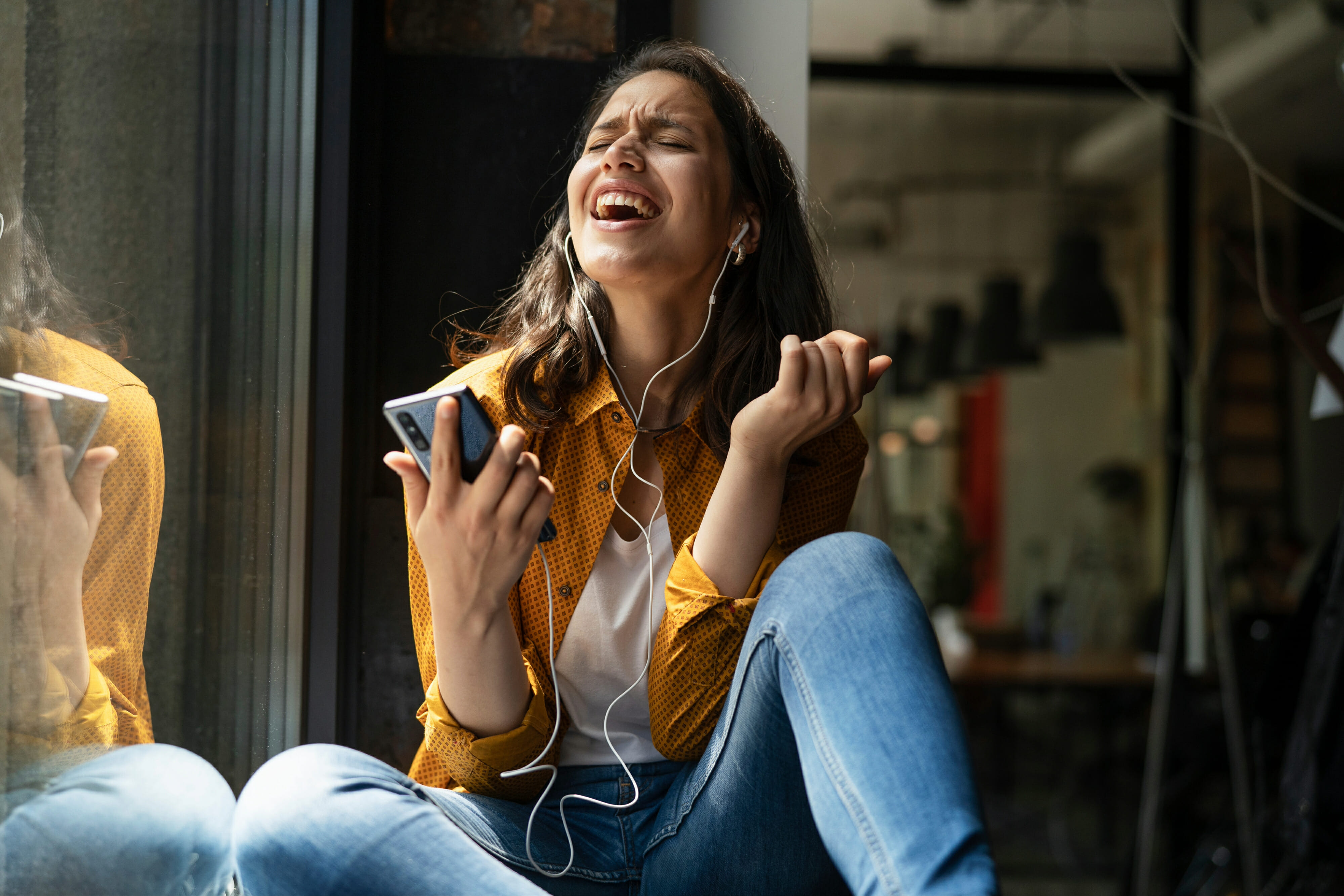 Young woman sitting and listening to music with earphones while singing a song