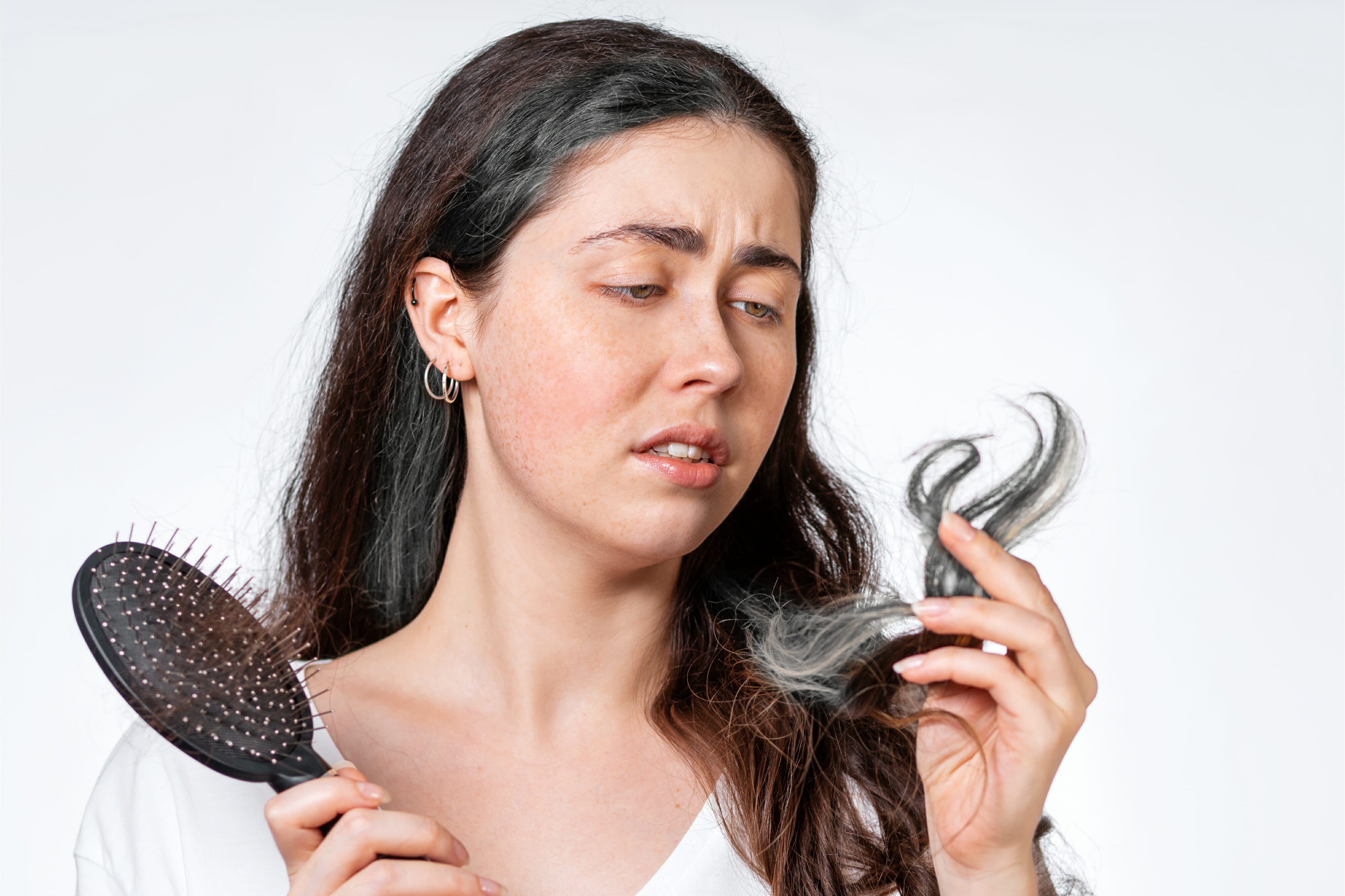 Woman holds a comb with her hair falling out and looks at the gray hair