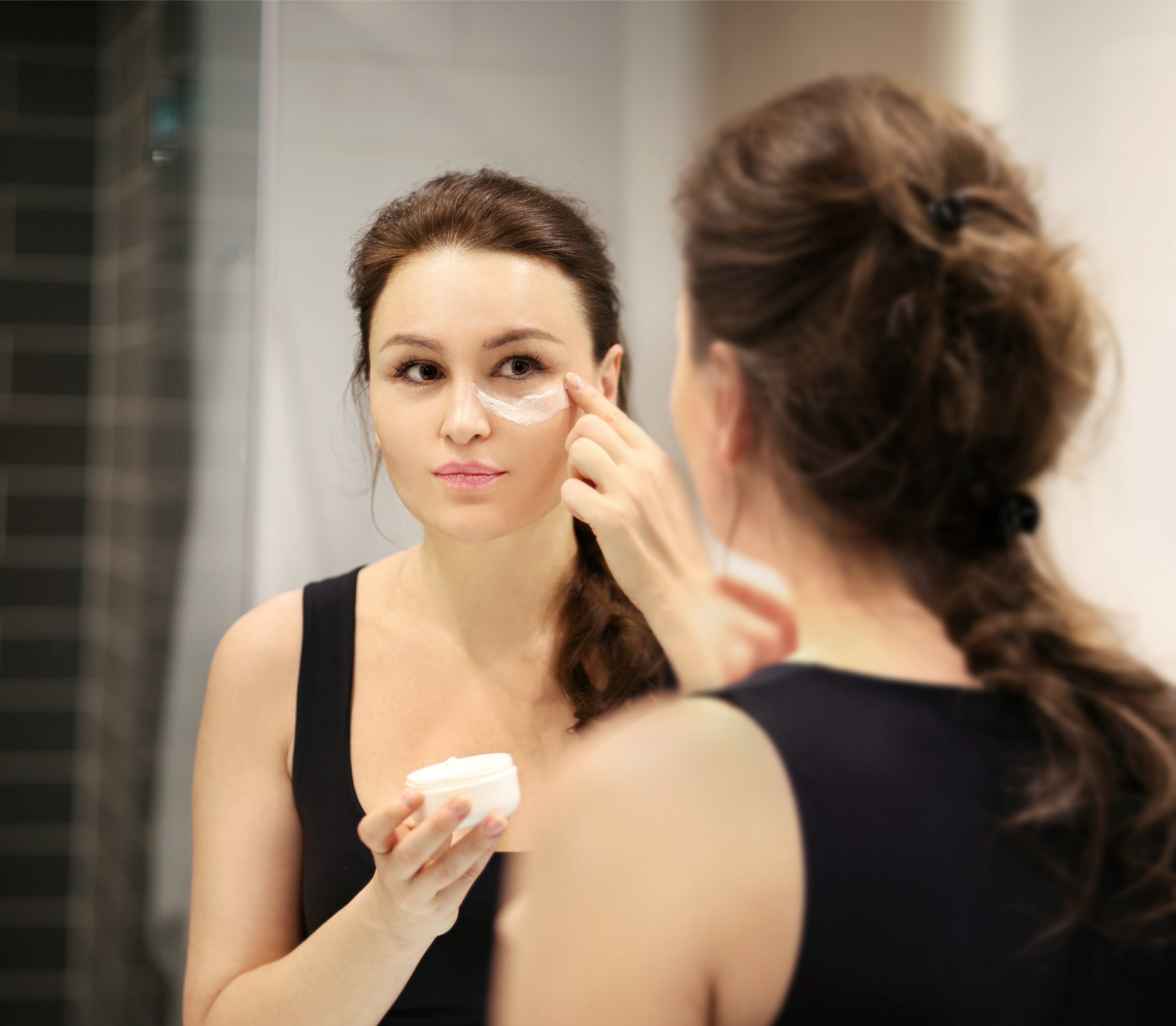 Woman applying anti-aging cream in the front mirror