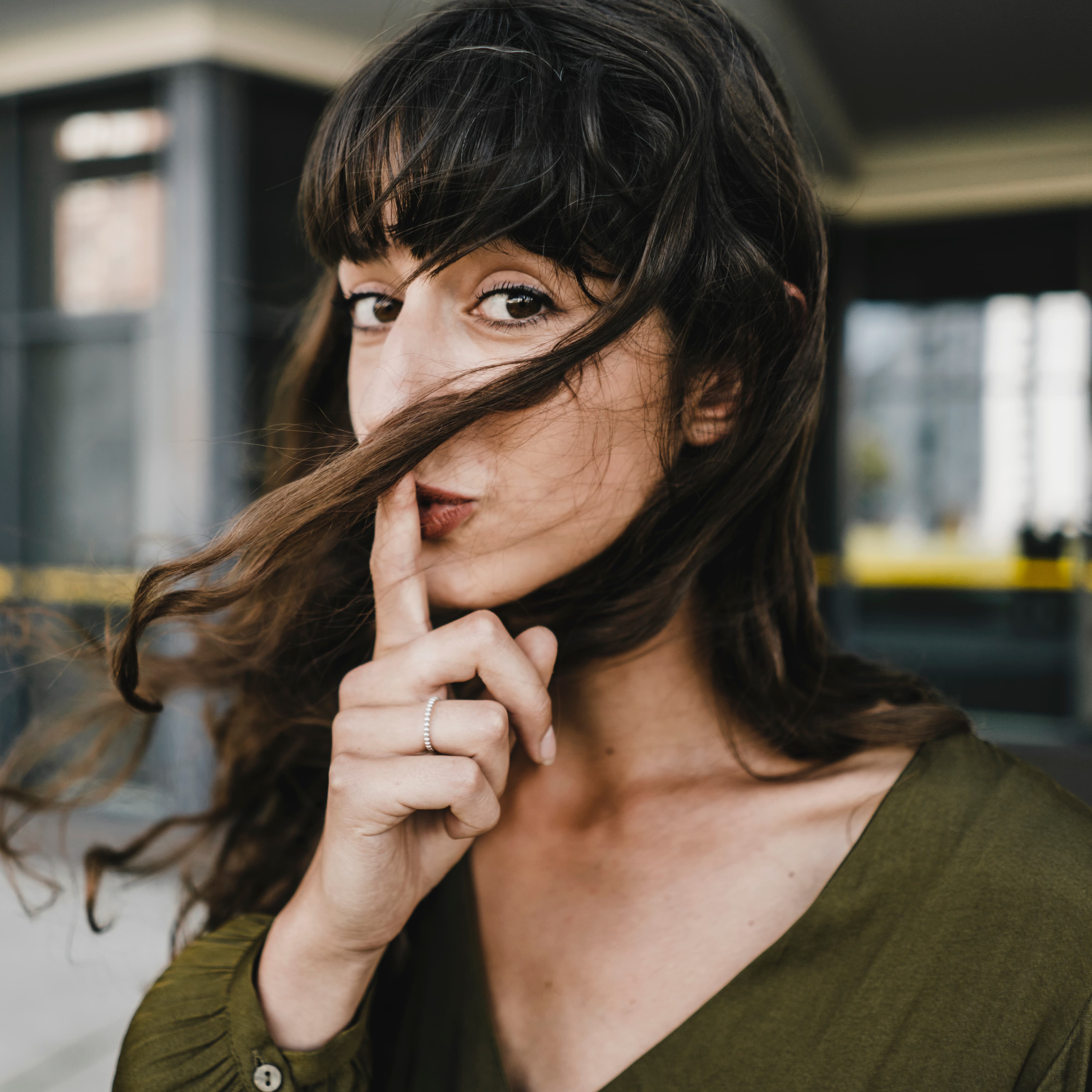 Portrait of smiling brunette woman, finger on mouth