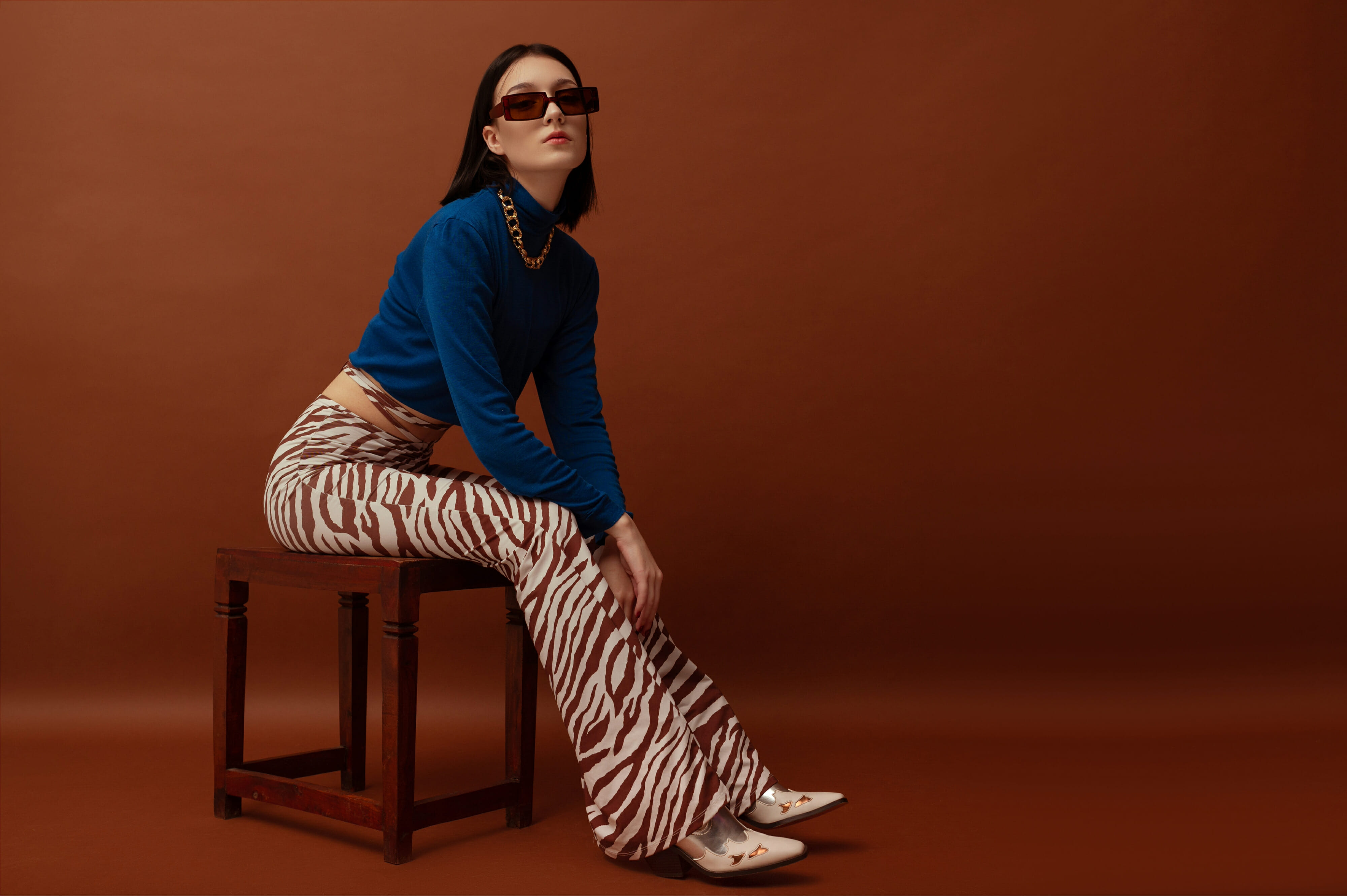 Fashionable woman wearing trendy brown rectangular sunglasses, stylish blue turtleneck, flared trousers with zebra print, and boots